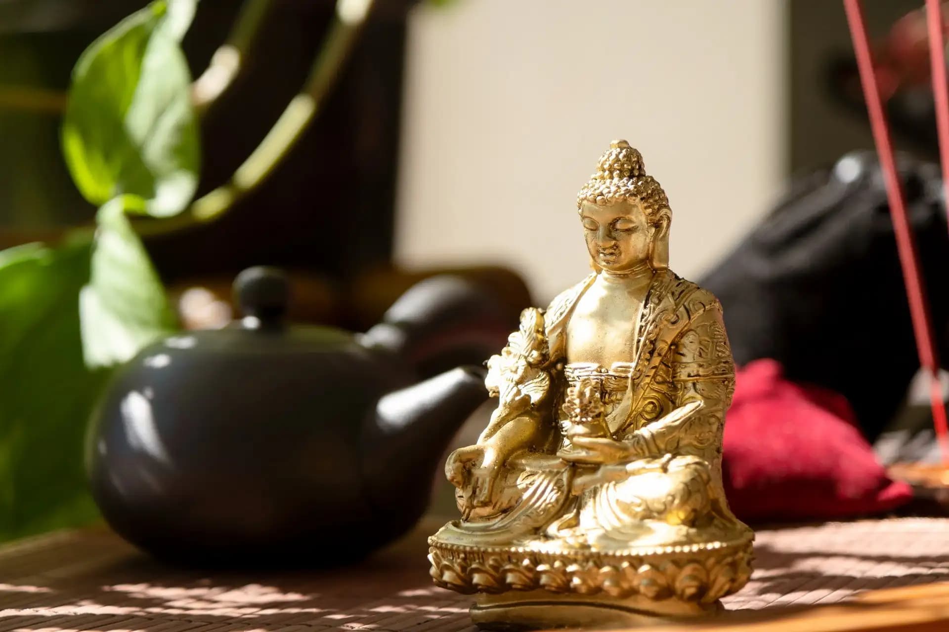 A golden Buddha statue beside a black teapot and incense, set in warm afternoon light
